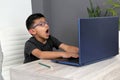 Boy with glasses does home schooling takes online classes at home with a laptop, studies, is surprised and participates in class