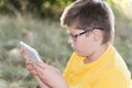 The boy in glasses looks tablet computer at nature