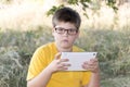 The boy in glasses looks tablet computer at nature