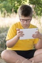 The boy in glasses looks tablet computer at nature