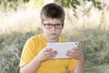 The boy in glasses looks tablet computer at nature