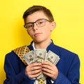 A boy in glasses and an oversized suit with a satisfied face is holding US dollars, a child and big money. Royalty Free Stock Photo