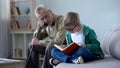 Boy in glasses reading book for grandfather, old man falling asleep on cosy sofa Royalty Free Stock Photo