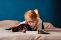 Boy with glasses reading a book next to his dog on the bed Royalty Free Stock Photo