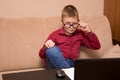 A boy in glasses and a red shirt sits at a black table and does homework, a child in quarantine on distance learning. he