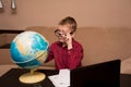 A boy in glasses and a red shirt is sitting at a black table looking at a geographical globe and doing homework, a child