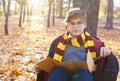 Boy in glasses stands in autumn park with gold leaves, holds book in his hands, wears in black robe Royalty Free Stock Photo