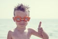 A boy in glasses for swimming shows a thumbs up on the background of the sea. Kid in spectacles for swimming in the sea Royalty Free Stock Photo