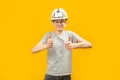 Boy with glasses wears protective helmet and shows thumbs up with two hands. Teenager shows gesture like, on yellow background