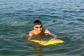 A boy in goggles learns to swim with a yellow inflatable mattress. Teenager swims in the sea with big splashes.