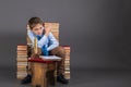 A boy with gold quill pen sitting in a throne of books