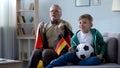 Boy and grandpa holding German flags, watching football, worrying about game