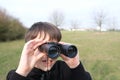 Boy, guy 8-10 years old stalker looks through black binoculars in the park, spies, hunts down secrets, the concept of surveillance Royalty Free Stock Photo