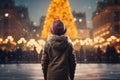 boy in a hat in the central square, looking at a large Christmas tree decorated for Christmas, rear view