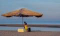 A boy in a hat and a girl on the beach with a suitcase under a straw umbrella look into the distance. Traveling of children Royalty Free Stock Photo