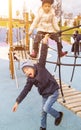 boy in hat is hanging on rope and his sister is standing behind and looking into camera. adorable children having fun playground Royalty Free Stock Photo