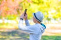 The boy in the hat takes pictures on a smartphone in the park