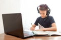 A boy in headphones in front of a computer does his homework. Distance learning in quarantine. Textbooks  are on the table Royalty Free Stock Photo