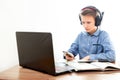 A boy in headphones in front of a computer does his homework. The boy is holding a phone. Distance learning in quarantine Royalty Free Stock Photo