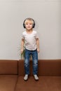 Boy in headphones jumps on couch. Child listens to music. Vertical frame