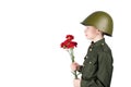 A boy in a helmet wearing a military uniform stands facing sideways and holding red flowers, isolated on white Royalty Free Stock Photo