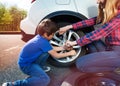 Boy helping mother to change tyre using lug wrench