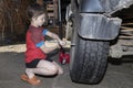 Boy helps to change the wheel of the car. Child works in the backyard of a house near the garage, sunny summer day. Side view