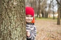 The boy hides behind a tree in the park. A child looks out from behind a tree, playing hide and seek on the street. Little boy is Royalty Free Stock Photo