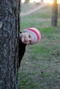 The boy hides behind a tree in the park. A child looks out from behind a tree, playing hide and seek on the street. Royalty Free Stock Photo