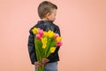 Boy hiding flowers of yellow and pink tulips behind itself, isolated on light orange background. Copy space