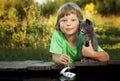Boy and his beloved kitten playing with a boat from pier in pond summer evening