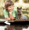 Boy and his beloved kitten playing with a boat from pier in pond summer evening Royalty Free Stock Photo