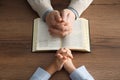 Boy and his godparent praying together at wooden table, closeup