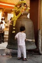 A boy hitting large outdoor Bell on top of hill in Wat Sangkas Ratanakhiri temple.