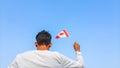 Boy holding Canada flag against clear blue sky. Man hand waving Canadian flag view from back, copy space