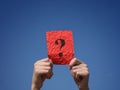 A boy holding a crumpled red paper note with a question mark on it in his hands against the blue sky Royalty Free Stock Photo