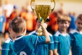 Boy holding golden trophy and celebrating sport success with team