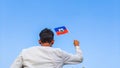Boy holding Haiti flag against clear blue sky. Man hand waving Haitian flag view from back, copy space