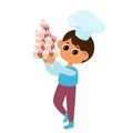 The boy is holding a lot of cupcakes or muffins in his hands. The child is happy and wearing a chef\'s hat.