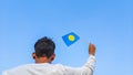 Boy holding Palau flag against clear blue sky. Man hand waving Palauan flag view from back, copy space