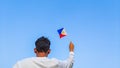 Boy holding Philippines flag against clear blue sky. Man hand waving Filipino flag view from back, copy space