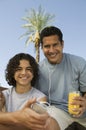 Boy (13-15) holding portable music player father listening with earphones an holding glass of juice front view portrait. Royalty Free Stock Photo