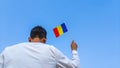 Boy holding Romania flag against clear blue sky. Man hand waving Romanian flag view from back, copy space Royalty Free Stock Photo