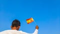 Boy holding Spain flag against clear blue sky. Man hand waving Spanish flag view from back, copy space