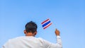 Boy holding Thailand flag against clear blue sky. Man hand waving Thai flag view from back, copy space