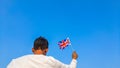 Boy holding Union Jack or United Kingdom flag against clear blue sky. Man hand waving UK flag view from back, copy space Royalty Free Stock Photo