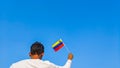 Boy holding Venezuela flag against clear blue sky. Man hand waving Venezuelan flag view from back, copy space