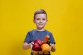 The boy holds a basket with fresh vegetables and fruits on a yellow background. Vegan and healthy concept