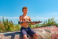 The boy holds a black clarinet in his hands, comprehending Zen sitting on an old wooden boat on the beach. Royalty Free Stock Photo