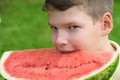 Boy holds a slice of red watermelon and wants to bite off a slice, side view close-up Royalty Free Stock Photo